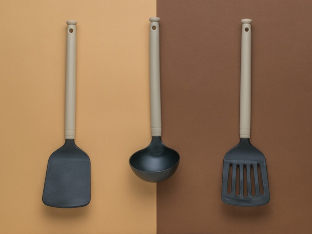 Deux spatules de cuisine et une louche sur fond bicolore. Mise à plat.