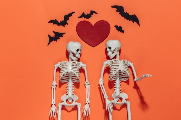 Deux squelettes, chauves-souris et coeur décoratif rouge sur fond orange vif. Thème de la Saint-Valentin ou d'halloween.