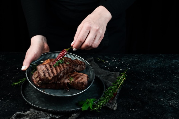 Deux steaks de boeuf ribeye grillés sur une assiette entre les mains du chef Bannière alimentaire Sur fond noir