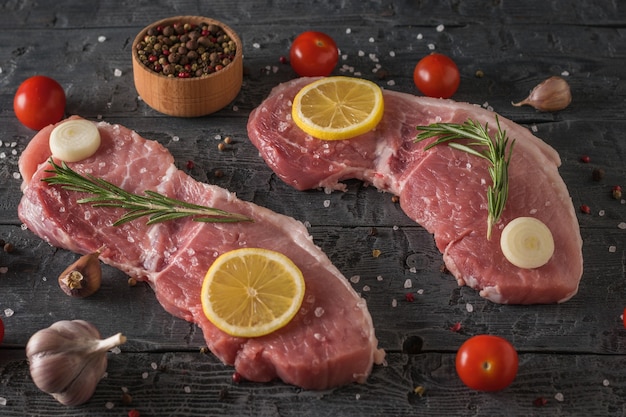 Deux steaks de porc aux épices et gros sel sur une table en bois noir. Ingrédients pour la cuisson des plats de viande.