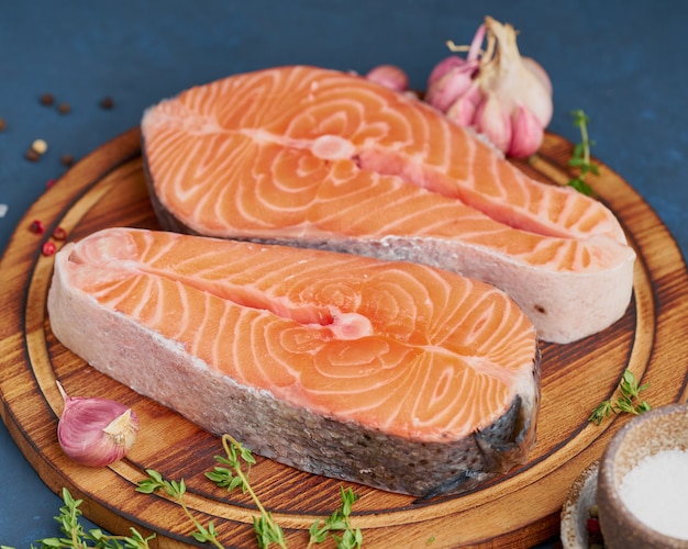 Deux steaks de saumon, filet de poisson, grandes tranches sur une planche à découper sur une table sombre. Vue de côté