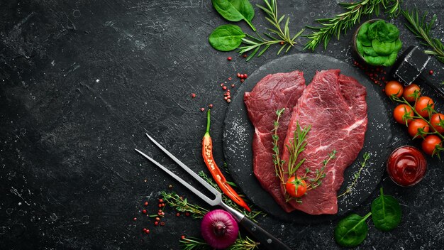 Deux steaks de veau crus au romarin et aux épices Sur fond de pierre noire Vue de dessus