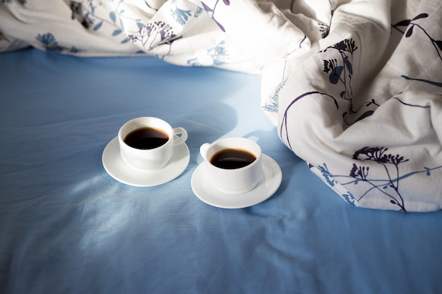 Deux tasses blanches de café sont au lit, matin ensoleillé