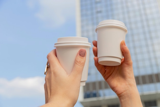 Deux tasses blanches avec du café pour aller dans les mains des femmes dans le contexte des bâtiments de la ville et du ciel