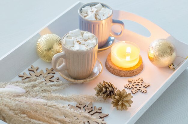 Deux tasses de boisson chaude avec des guimauves et un décor de Noël sur un plateau en bois blanc