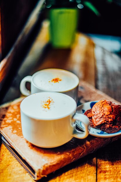 Photo deux tasses de café au cappuccino et des biscuits au brownie sur la table en bois.