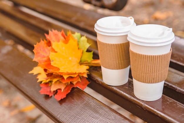 Deux tasses à café au parc du banc de la ville avec bouquet de feuilles d'érable jaunes