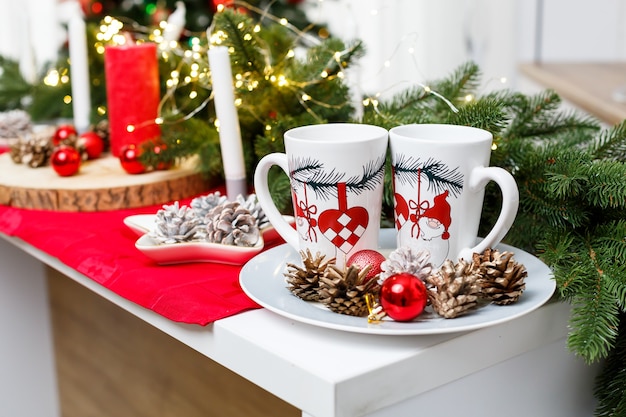 Deux tasses à café blanches sur la table de la cuisine sur fond de décorations de Noël. Morceaux sur un plateau