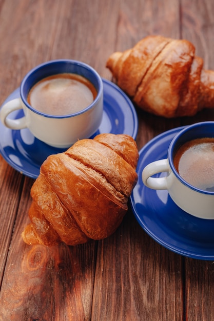 Deux tasses de café et des croissants sur un fond en bois, bonne lumière, atmosphère du matin