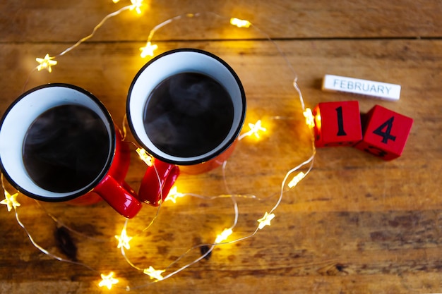 Deux tasses de café dans des tasses rouges sur un mur de guirlandes. Petit déjeuner le matin pour la Saint Valentin. Concept d'amour.