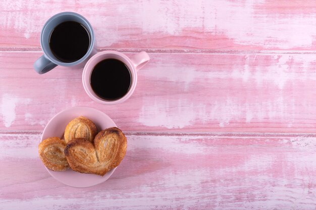 Deux tasses de café avec deux pâte feuilletée coeur sur un bois rose pour un petit déjeuner romantique