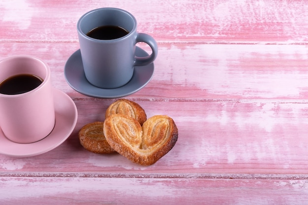 Deux tasses de café avec deux pâte feuilletée coeur sur un bois rose pour un petit déjeuner romantique