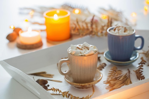 Deux tasses de café avec des guimauves et un décor d'automne sur un plateau en bois blanc