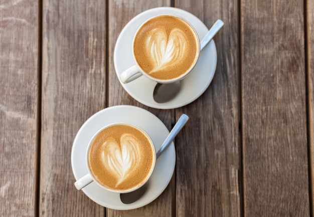 Deux tasses de café avec motif coeur dans une tasse blanche sur fond de bois