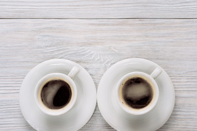 Deux tasses de café avec de la mousse sur une table en bois blanche