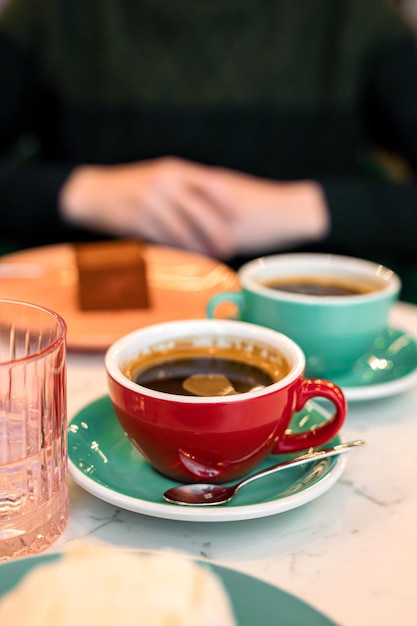 Deux tasses de café noir, un verre d'eau et un dessert. Un homme en arrière-plan. Au café, image lifestyle