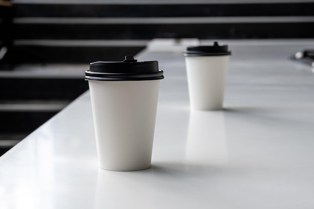 Deux tasses de café en papier blanc sur une table blanche.