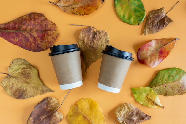 Deux tasses à café en papier avec couvercles en feuilles d'automne avec fond orange