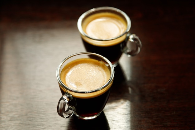 Deux tasses à café en verre avec expresso près de la fenêtre le matin sur fond sombre