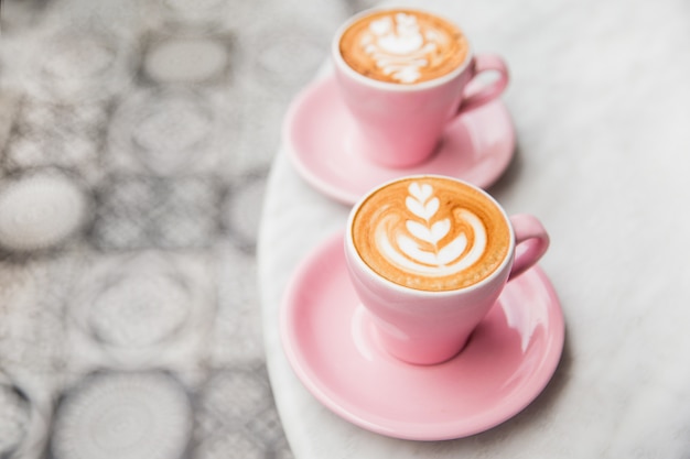 Photo deux tasses de cappuccino rose avec un bel art latte sur table en marbre.