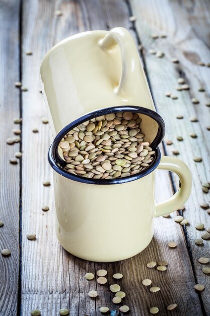 Deux tasses avec des lentilles vertes biologiques sur fond de bois