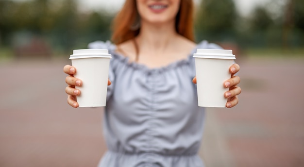 Deux tasses en papier blanc avec du café dans la main de la femme. Il est temps de boire un café en ville. Café à emporter. Profitez du moment, faites une pause. Gros plan de la tasse de papier jetable. Délicieuse boisson chaude. Espace vide pour le texte,