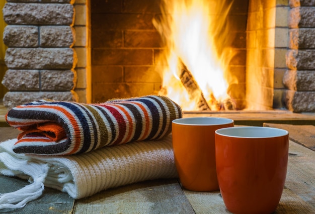 Photo deux tasses pour le thé ou le café, choses de laine près de la cheminée, dans la maison de campagne, vacances d'hiver