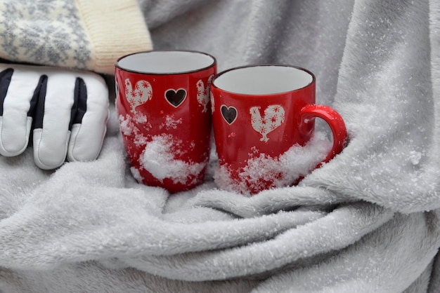 Deux tasses rouges en forme de coeur sur un plaid avec de la neige et des gants et un fond de chapeau