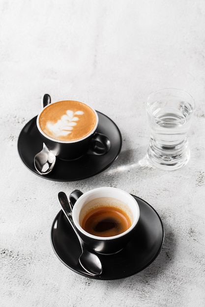 Deux tasses sombres de café noir chaud, expresso, cappuccino avec du lait isolé sur fond de marbre brillant. Vue aérienne, espace copie. Publicité pour le menu du café. Menu du café. Photo verticale.