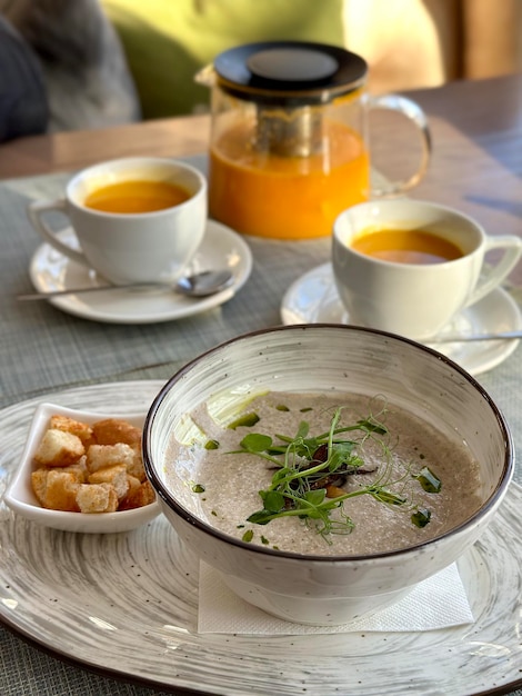 Deux tasses de thé à l'argousier avec une théière et une assiette de soupe aux champignons avec des craquelins