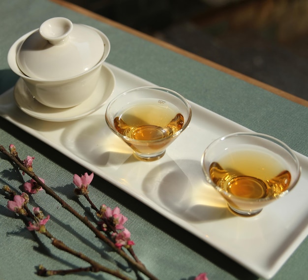 Deux tasses de thé et un bol de fleur de prunier sont posés sur une table.