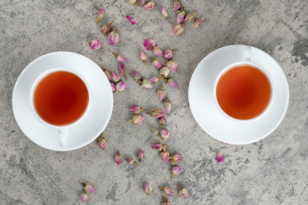 Deux tasses de thé noir avec des fleurs séchées sur marbre.