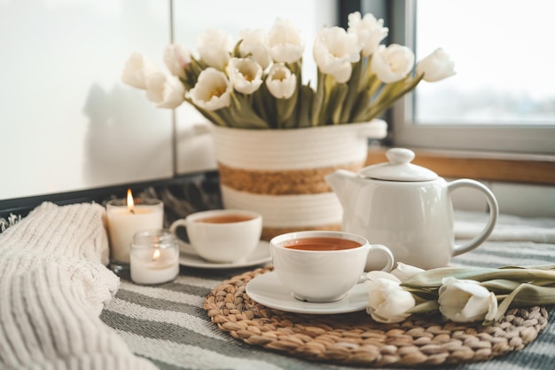 Deux tasses de thé un panier en osier avec des tulipes brûlant des bougies un chandail intérieur de la maison