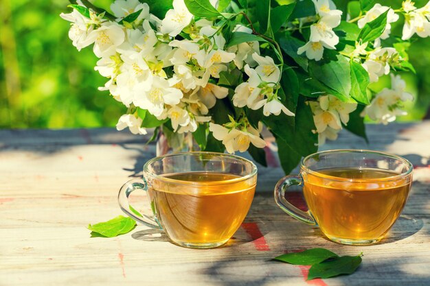 Deux tasses de thé vert avec des fleurs de jasmin sur une table en bois grunge à l'extérieur