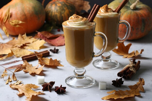 Deux tasses en verre latte citrouille aux épices sur table grise avec citrouilles et feuilles d'automne, gros plan.