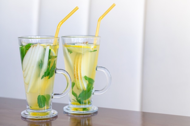 Deux tasses en verre de thé aux fruits à la menthe, citron, poire, miel et gingembre sur table en bois