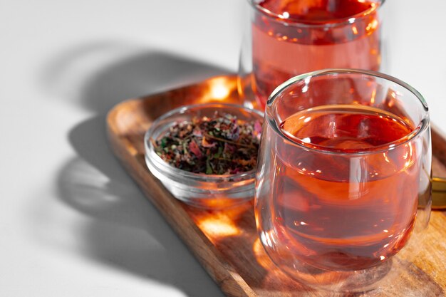 Deux tasses en verre de thé aux fruits sur plateau en bois sur table blanche close up
