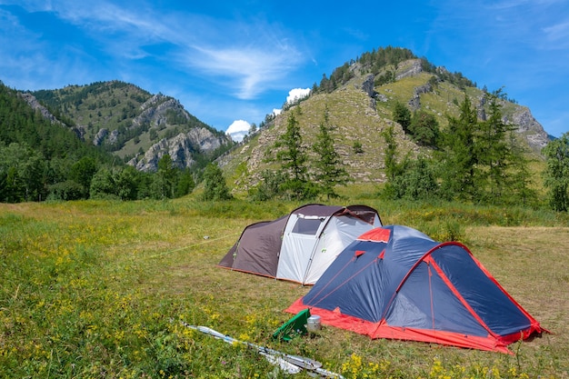 Deux tentes ouvertes se dressent sur l'herbe près des montagnes. Rames à proximité du bateau. Camp de rafting.