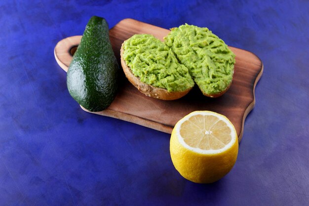 Deux toasts d'avocat vert frais sur une planche de bois Toasts un demi-avocat et un citron jaune dans une peau sur un fond bleu Gros plan