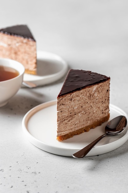 Deux tranches de gâteau au fromage au chocolat sur des assiettes blanches avec une tasse de thé sur fond blanc Copier l'espace