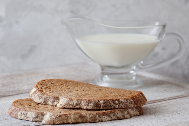 Deux tranches de pain noir, une cruche de lait sur une table en bois et un gris