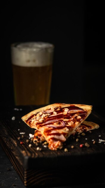 Photo deux tranches de pizza sur fond d'un verre de bière sur une planche de bois