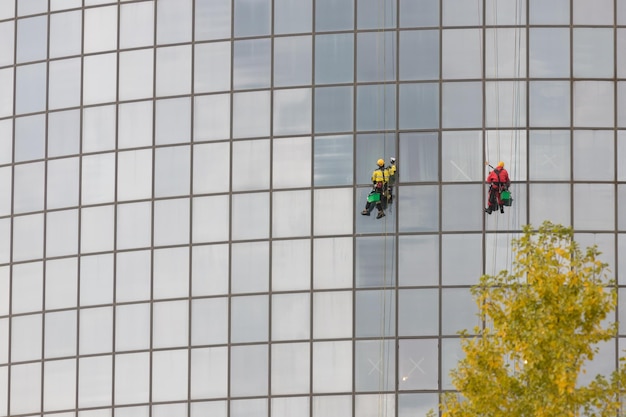 Deux travailleurs hommes nettoyant les fenêtres extérieures d'un gratte-ciel d'alpinisme industriel suspendu à des cordes