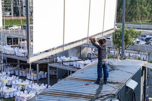 Deux travailleurs installent un panneau d'affichage extérieur en toile sur le toit du conteneur