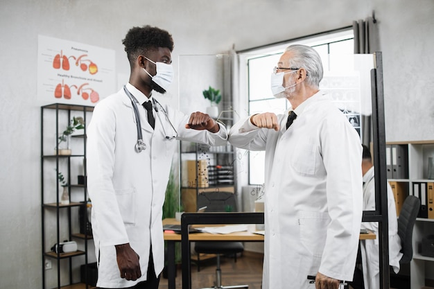 Deux travailleurs médicaux dans des masques faciaux saluant avec les coudes