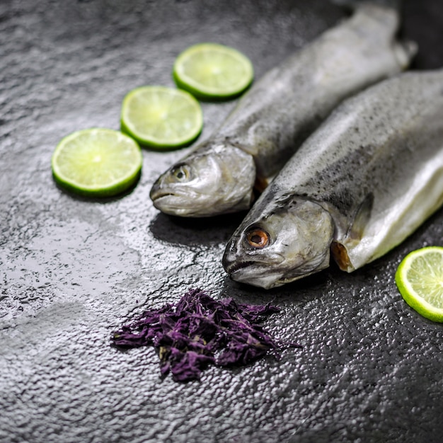 Deux truites de rivière crues aux herbes et au citron vert sur une pierre noire texturée