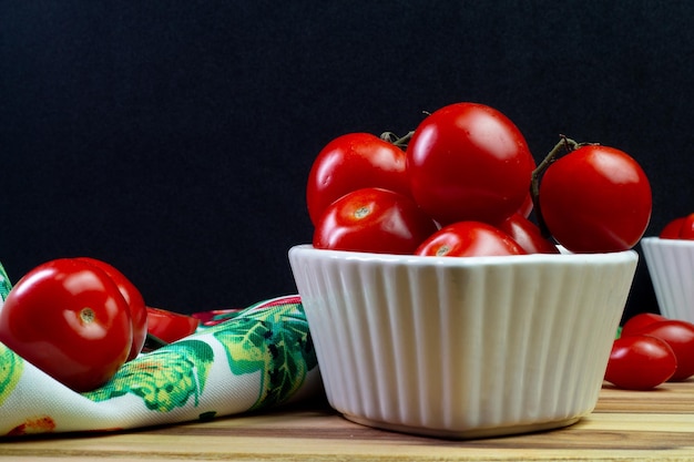 Deux types de tomates à l'intérieur d'un bol blanc sur une table en bois avec un fond noir