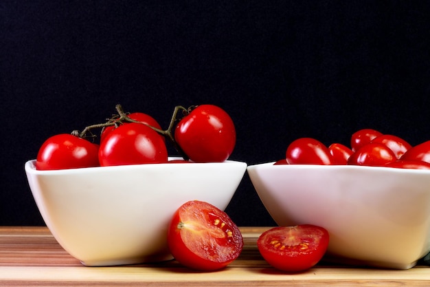 Deux types de tomates à l'intérieur d'un bol blanc sur une table en bois avec un fond noir