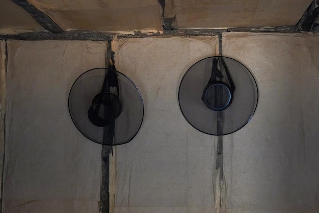 Deux ventilateurs noirs sont accrochés à un mur, dont l'un est recouvert de plastique noir.
