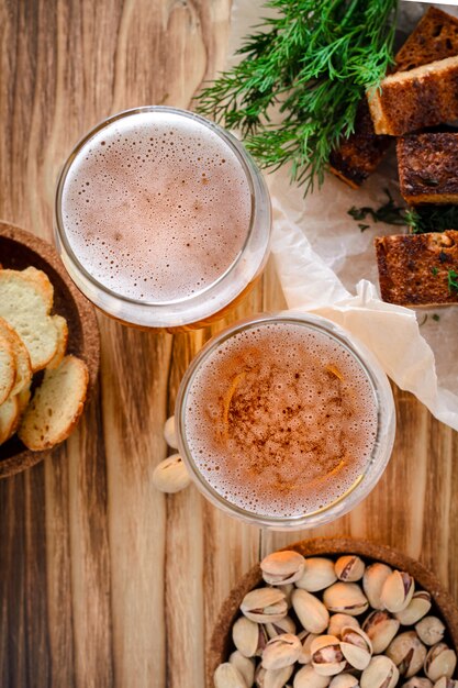 Deux verres de bière légère et des collations, des pistaches et des croûtons sur une table en bois